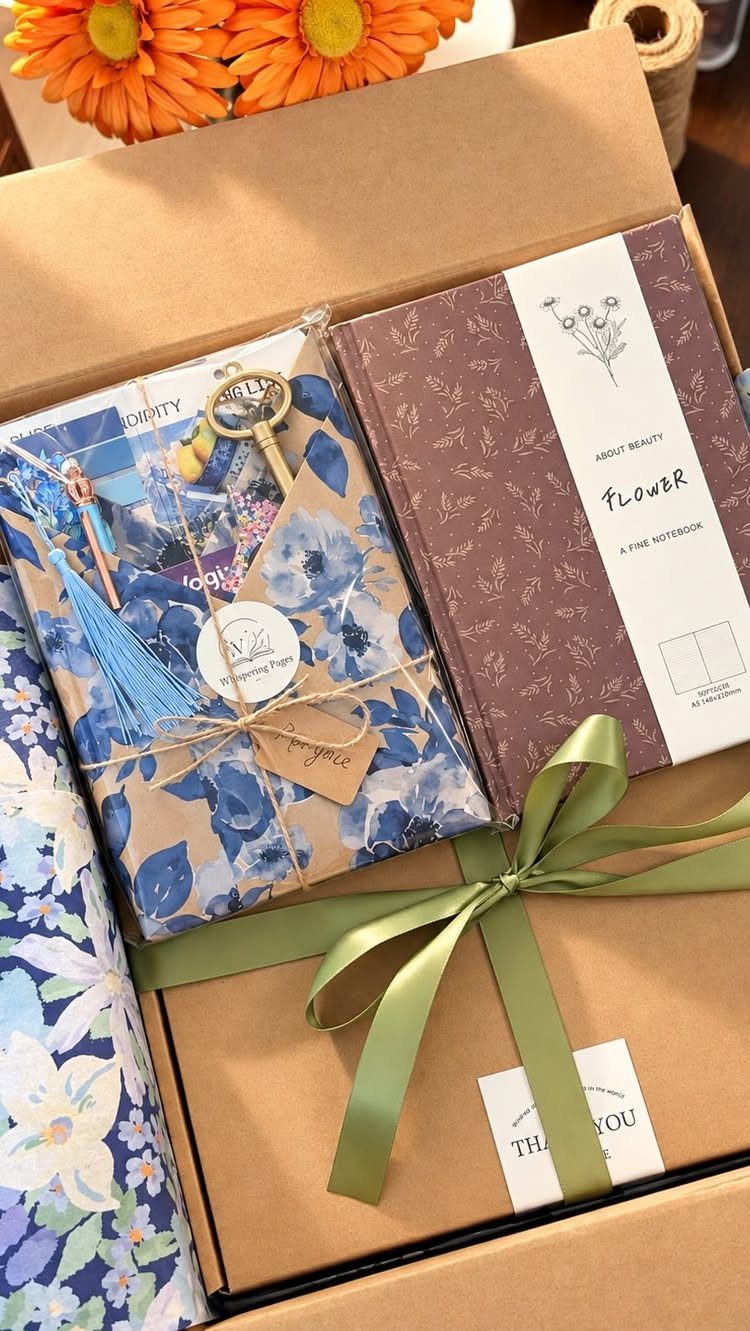 Gift box with a brown notebook, floral wrapped items, and a green ribbon.