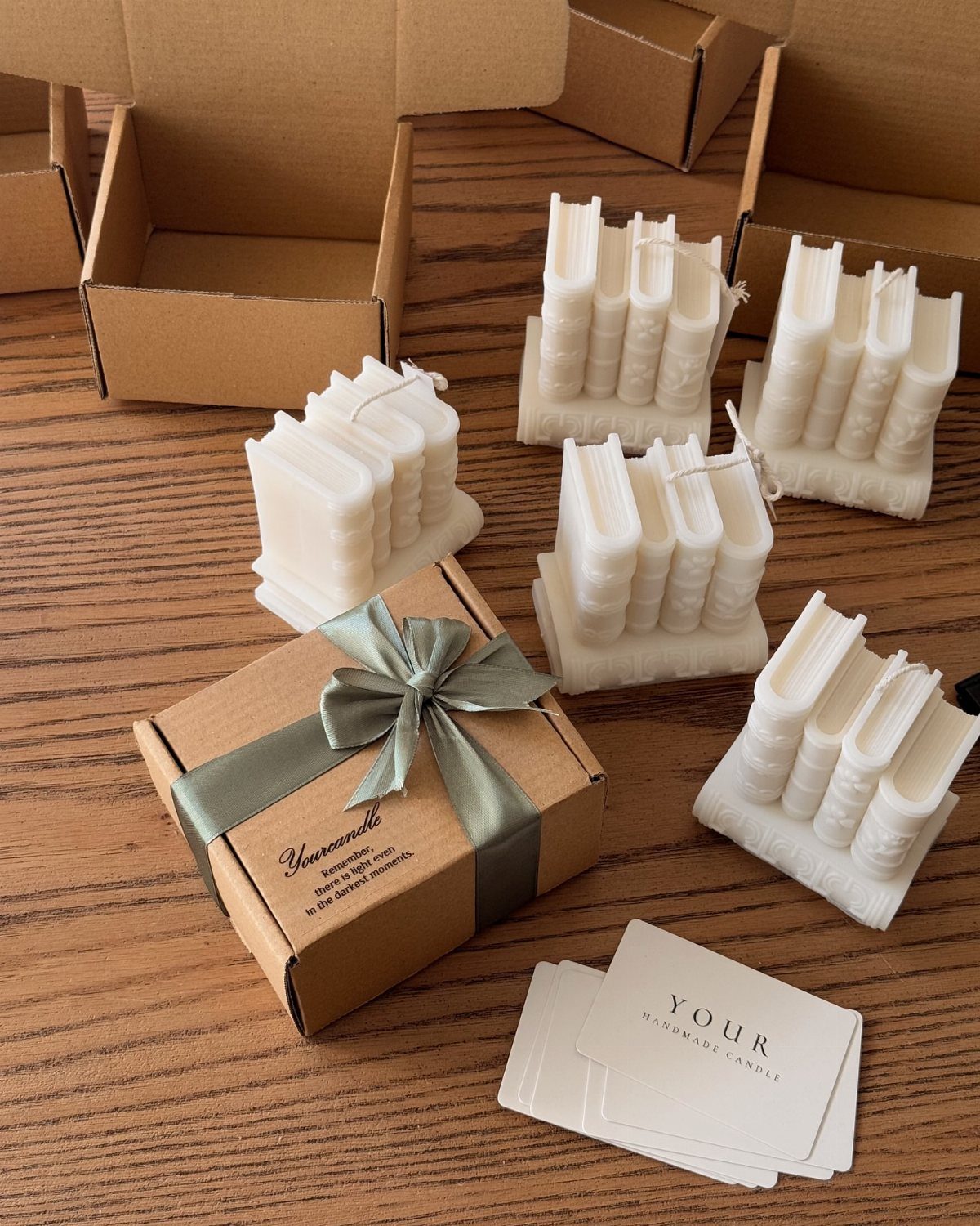 White wax candles shaped like books next to a gift box with ribbon.