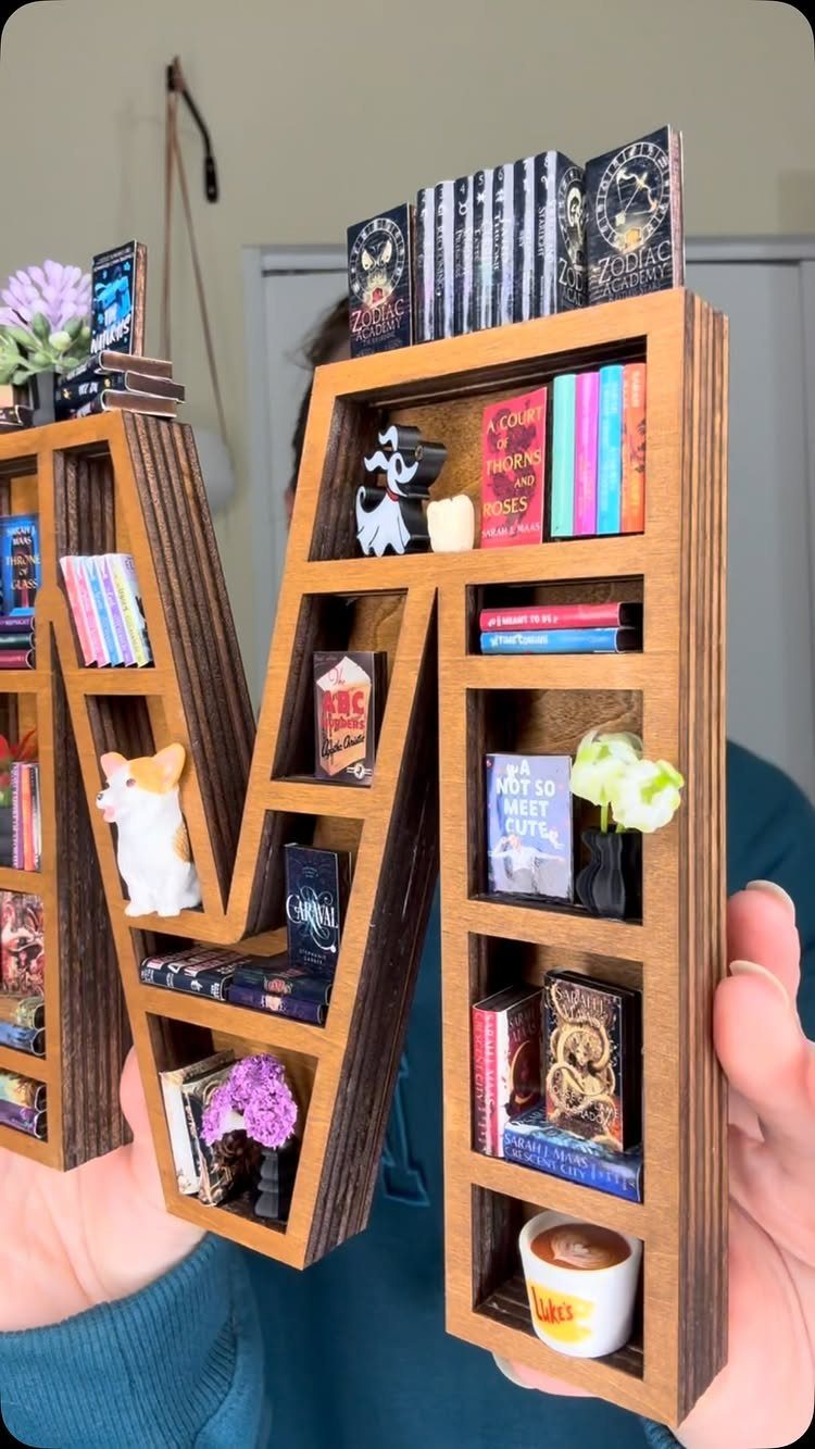 Wooden M-shaped miniature bookshelf filled with tiny books and small decorative figurines.