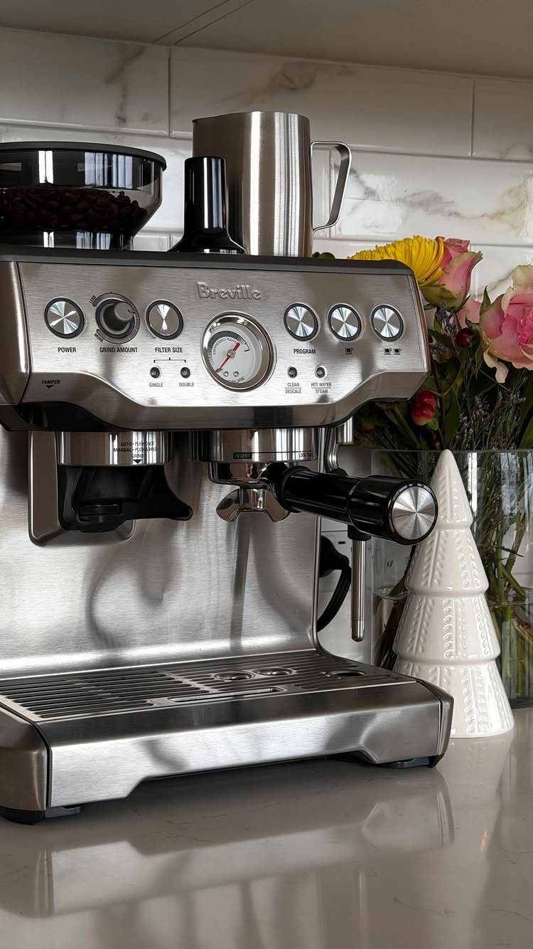 Breville espresso machine with built-in grinder on a white kitchen countertop with flowers.