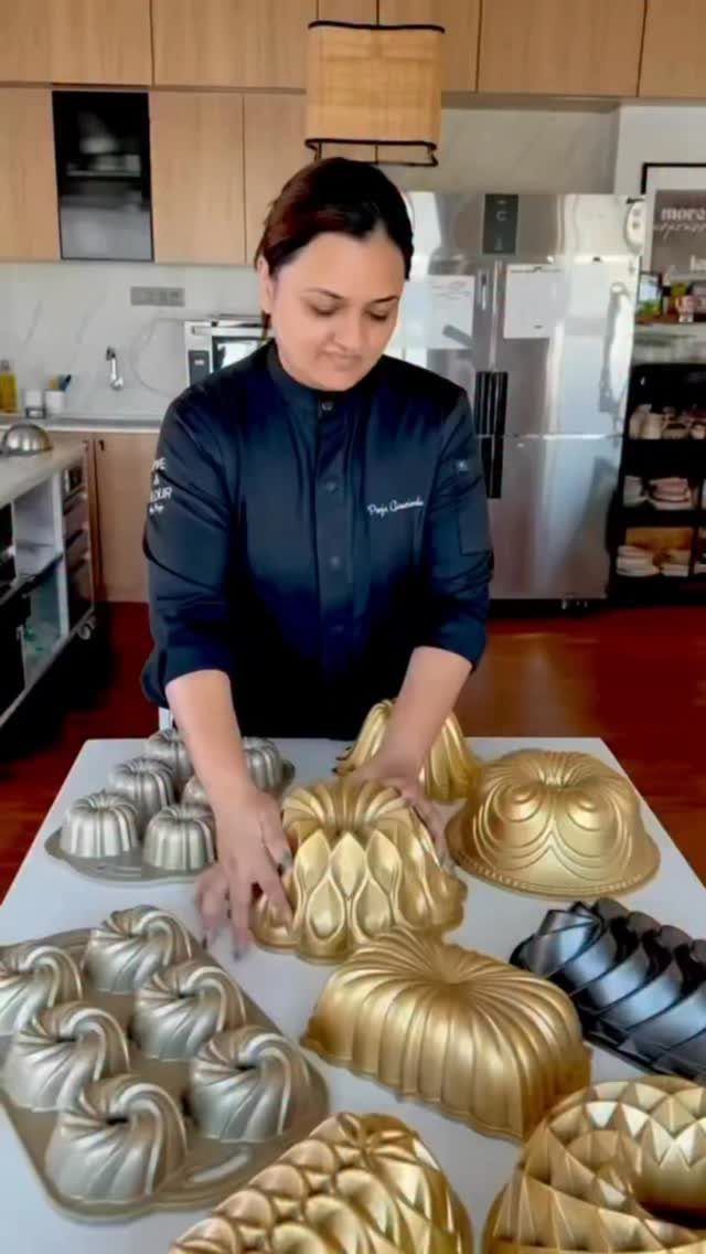 Chef in black coat standing behind a collection of gold and silver cake molds.