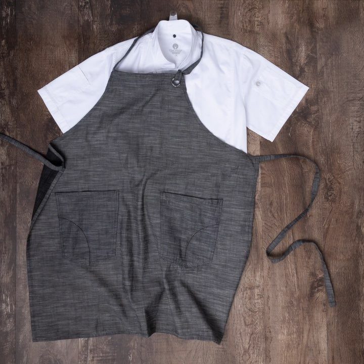 Grey fabric apron and white chef coat laid flat on a wooden background