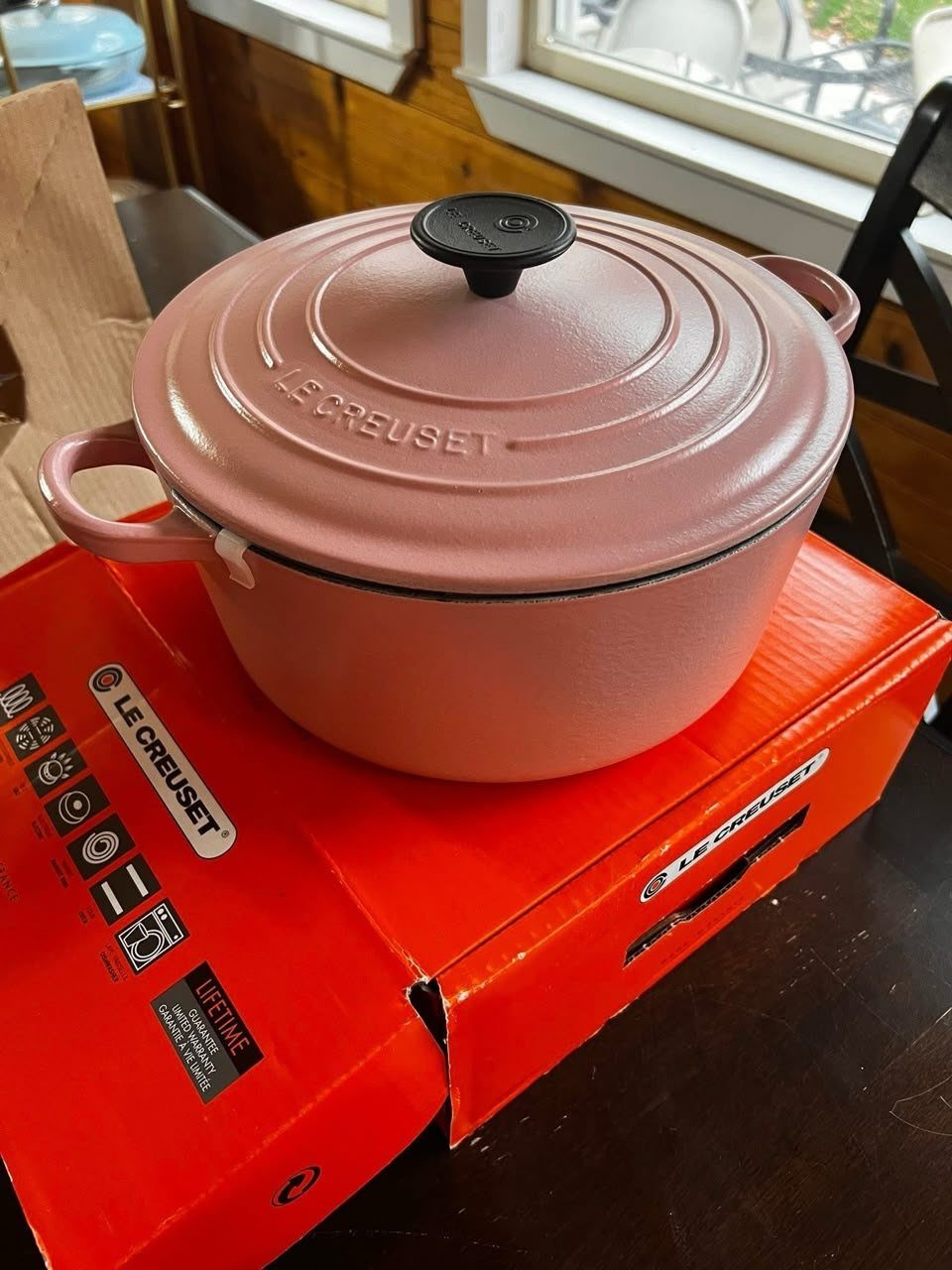 Pink Le Creuset Dutch oven sitting on its red branded packaging box.