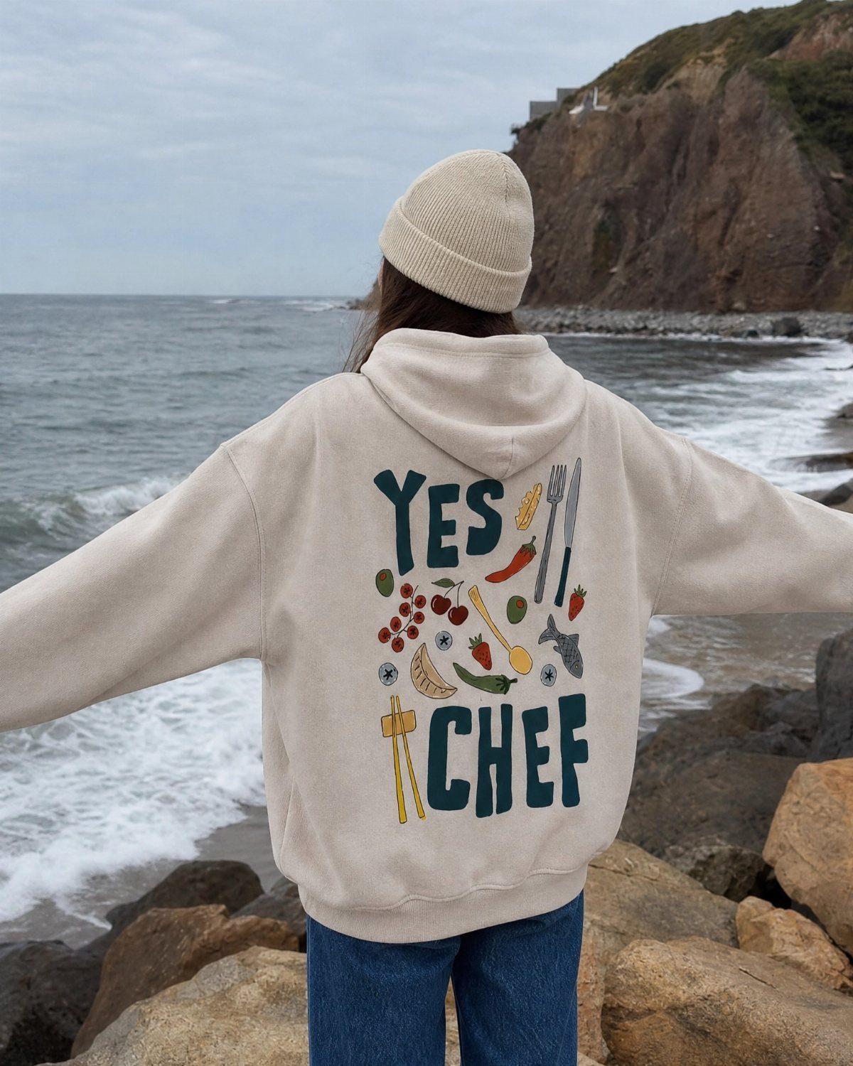 Person wearing a beige hoodie with Yes Chef text and cooking illustrations outdoors