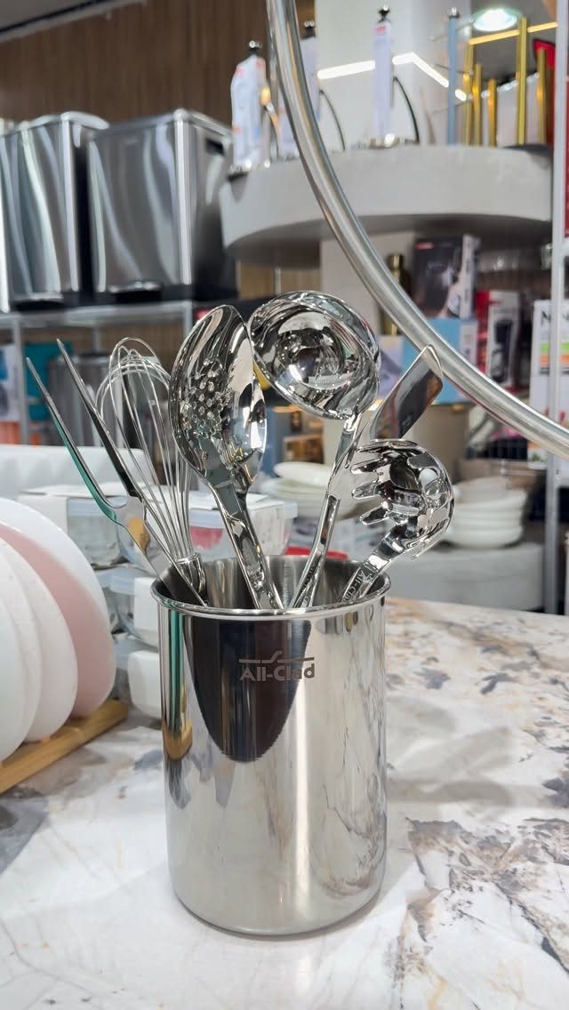 Stainless steel kitchen utensil holder with ladles and whisks on marble countertop