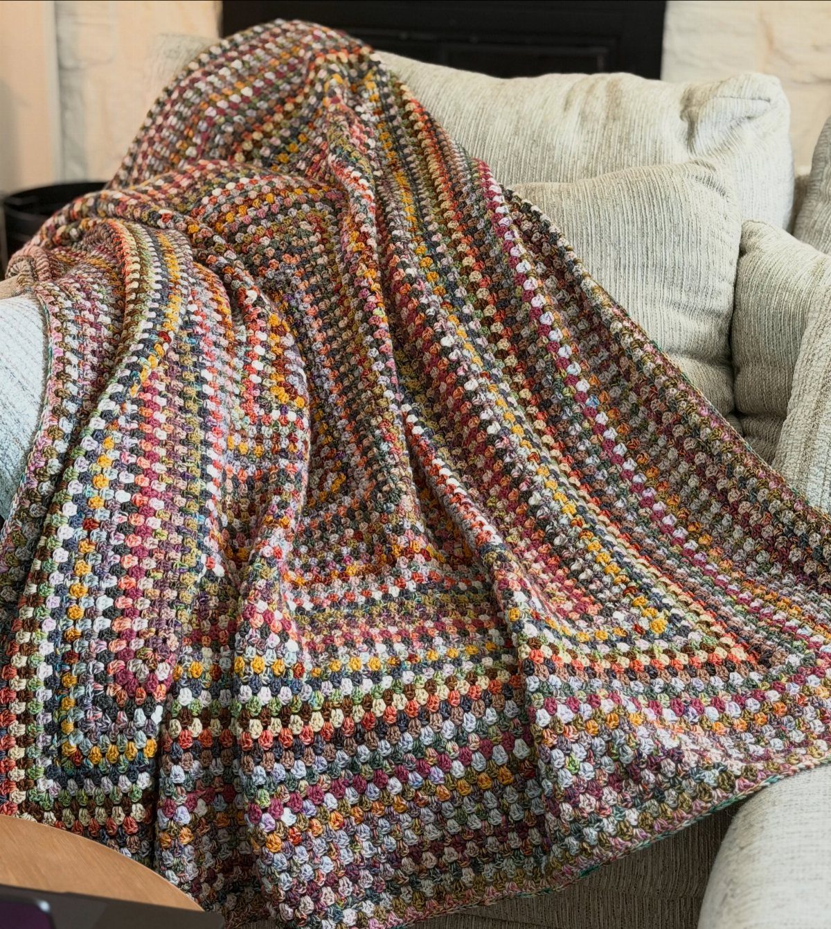 Multi-colored crocheted blanket draped over a light grey fabric sofa in a room.