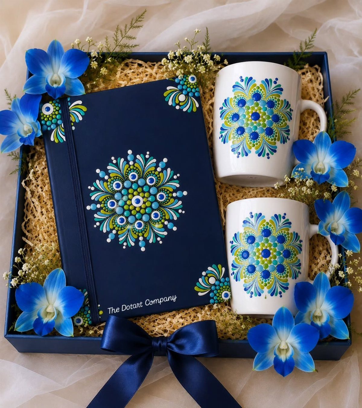Gift set with dot-painted notebook and mugs surrounded by blue orchids in a box