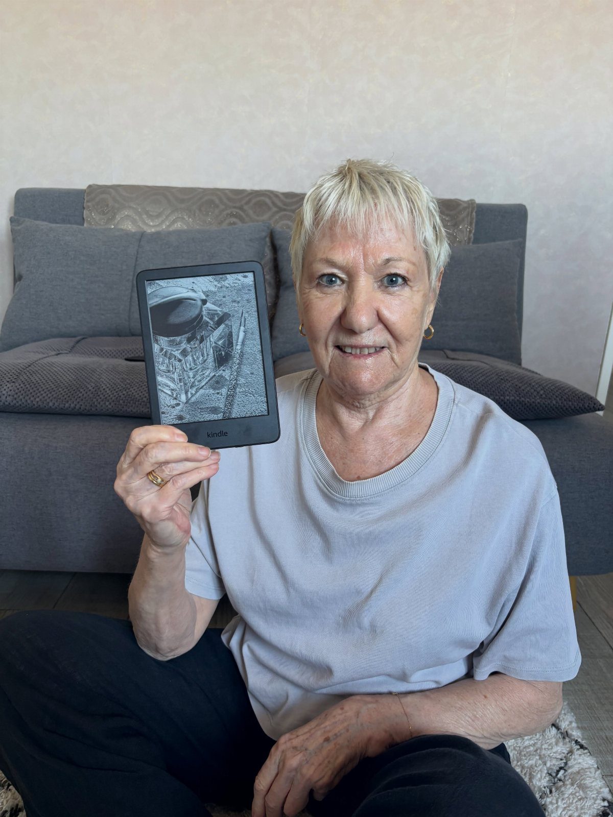 Elderly woman holding a black Kindle e-reader while sitting in a living room.