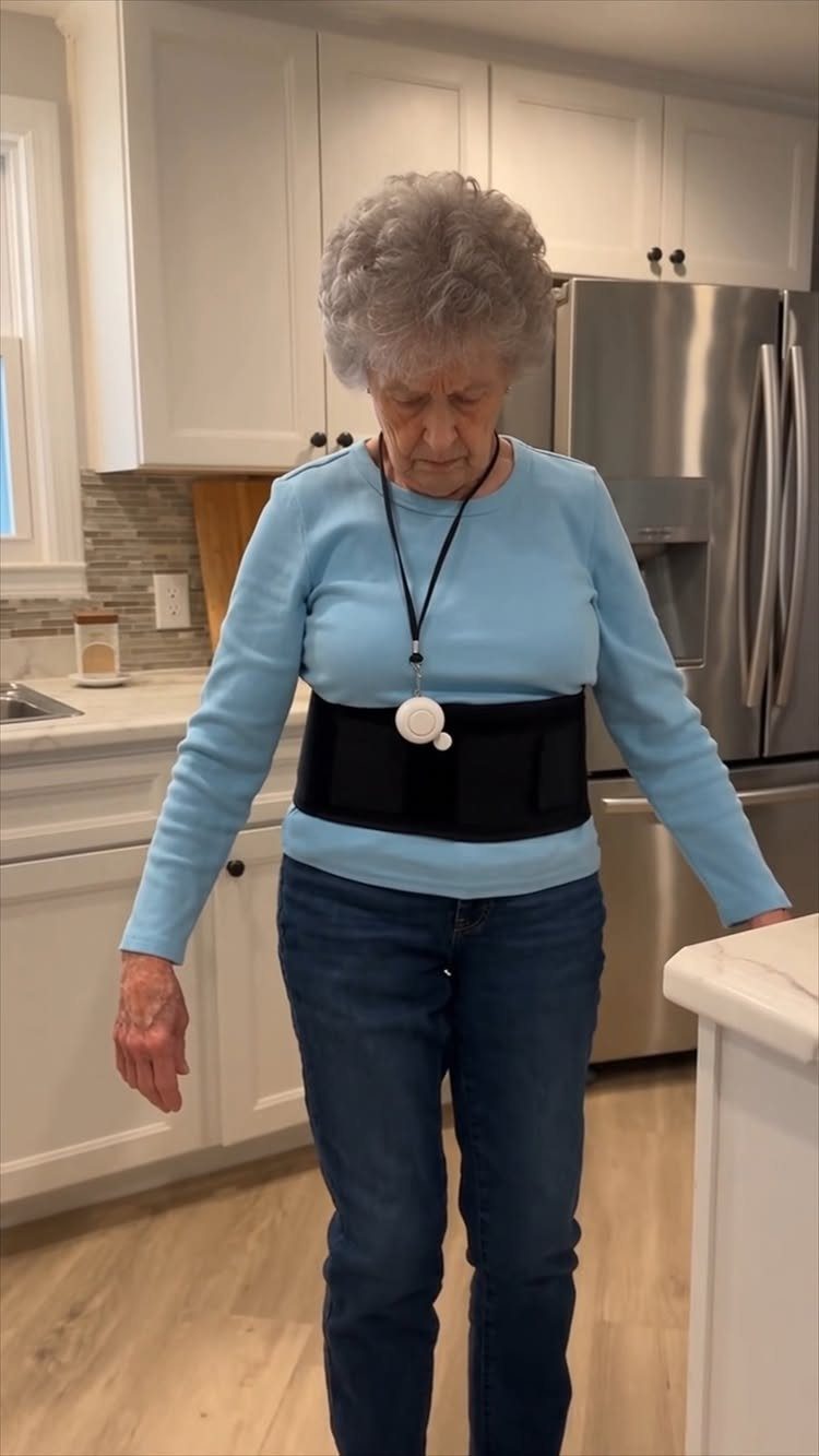 Elderly woman wearing a personal emergency response system pendant and waist belt in kitchen
