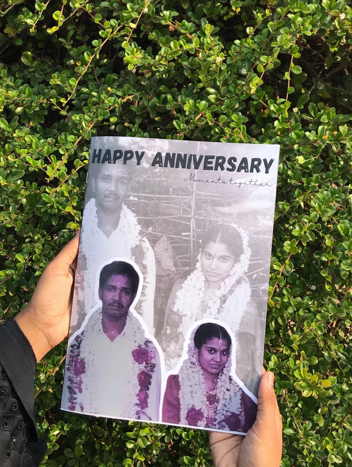 Personalized photo album cover with anniversary photos held against a green hedge background.