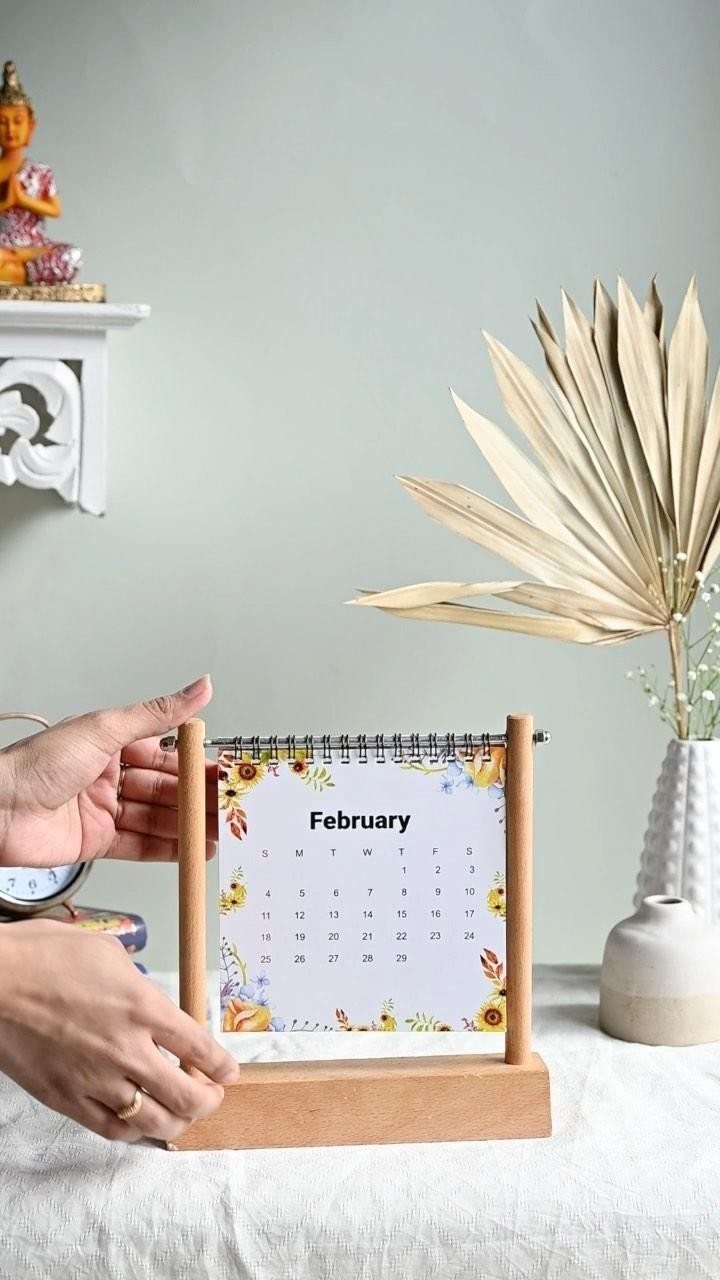 Wooden desk calendar with floral February page held by two hands on a table