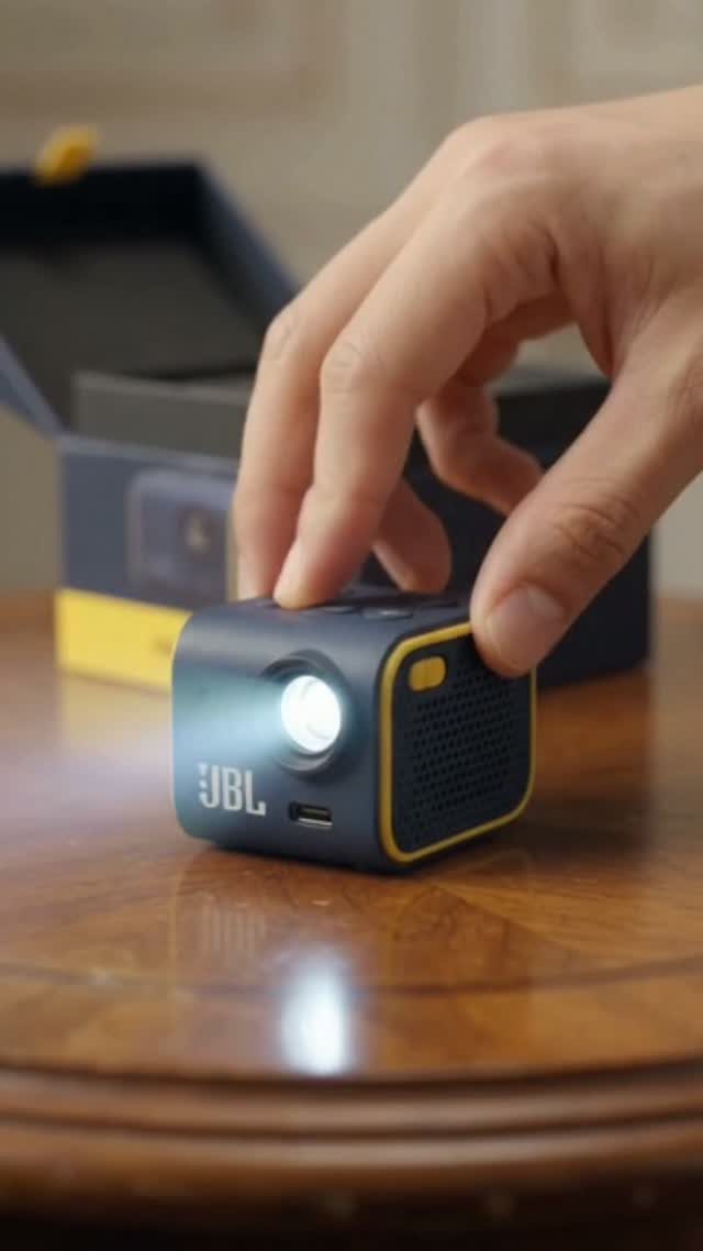 Hand touching a small JBL portable speaker with a bright light on a table