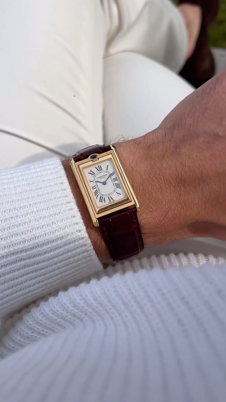 Gold rectangular watch with brown leather strap on a man's wrist