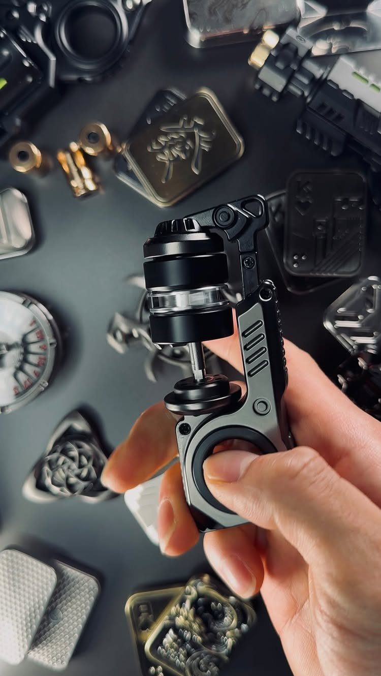 Hand holding a mechanical black and silver fidget toy among various metal gadgets.