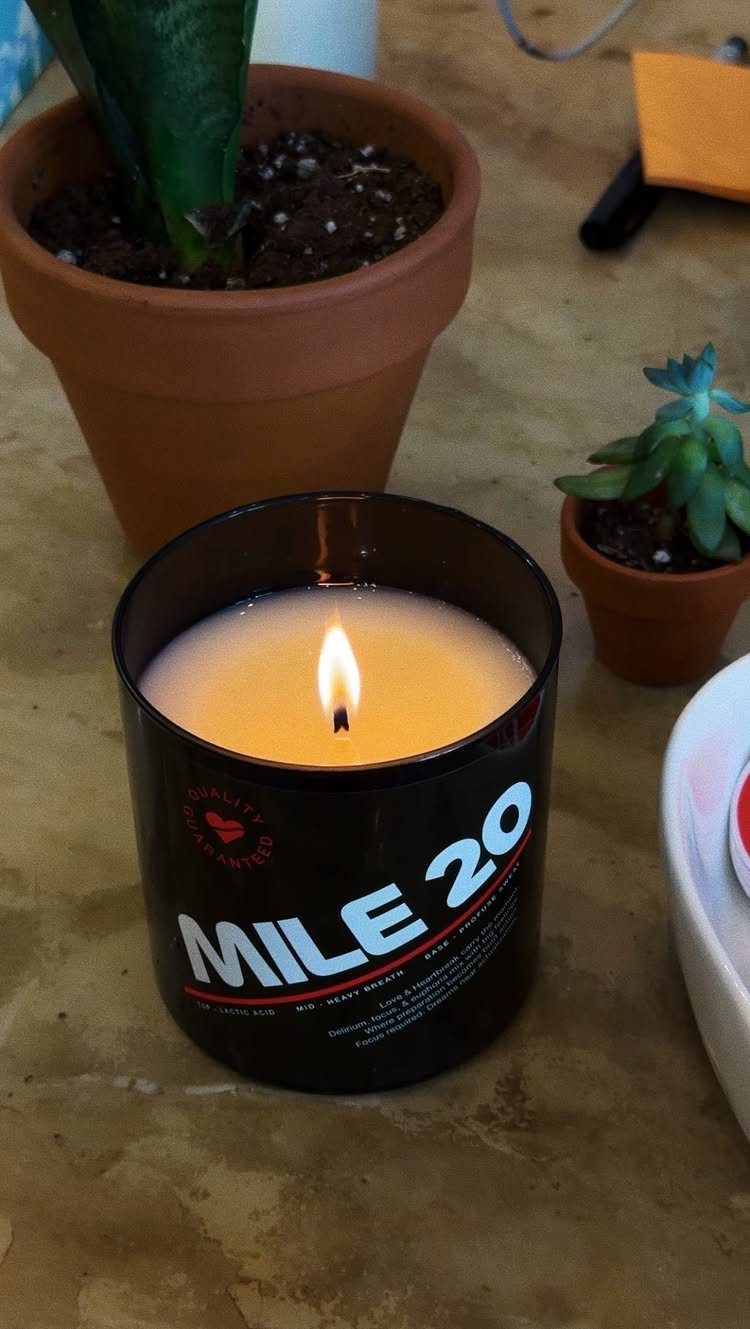 Lit candle in a black jar labeled Mile 20 next to small succulents