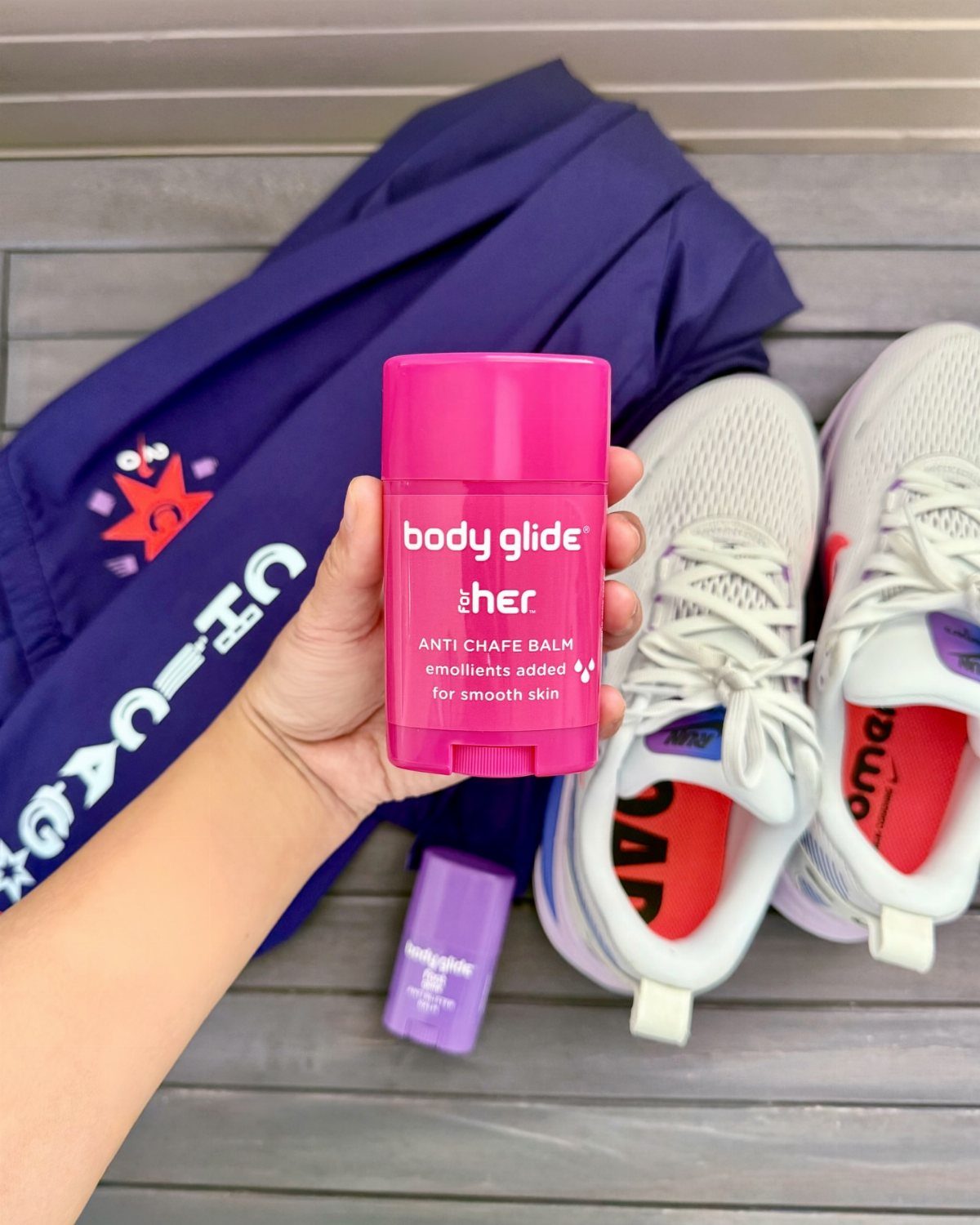 Pink anti-chafe balm stick held in hand next to white running shoes