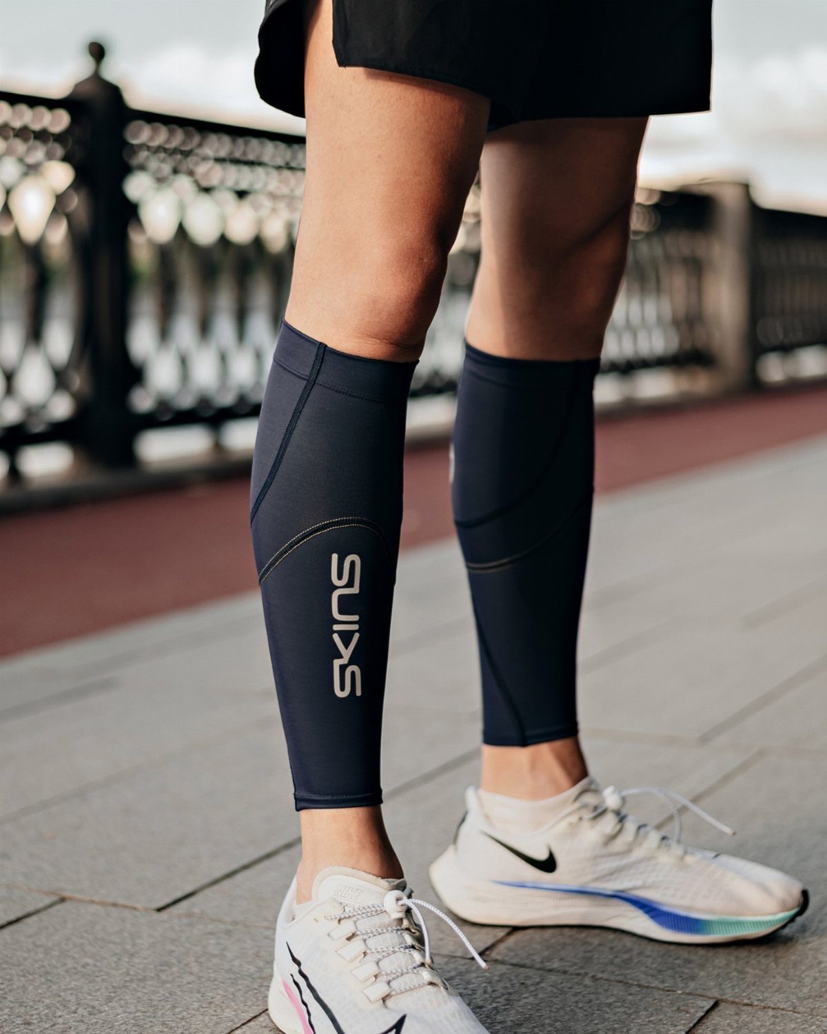 Person wearing dark blue compression calf sleeves and white running shoes on pavement.