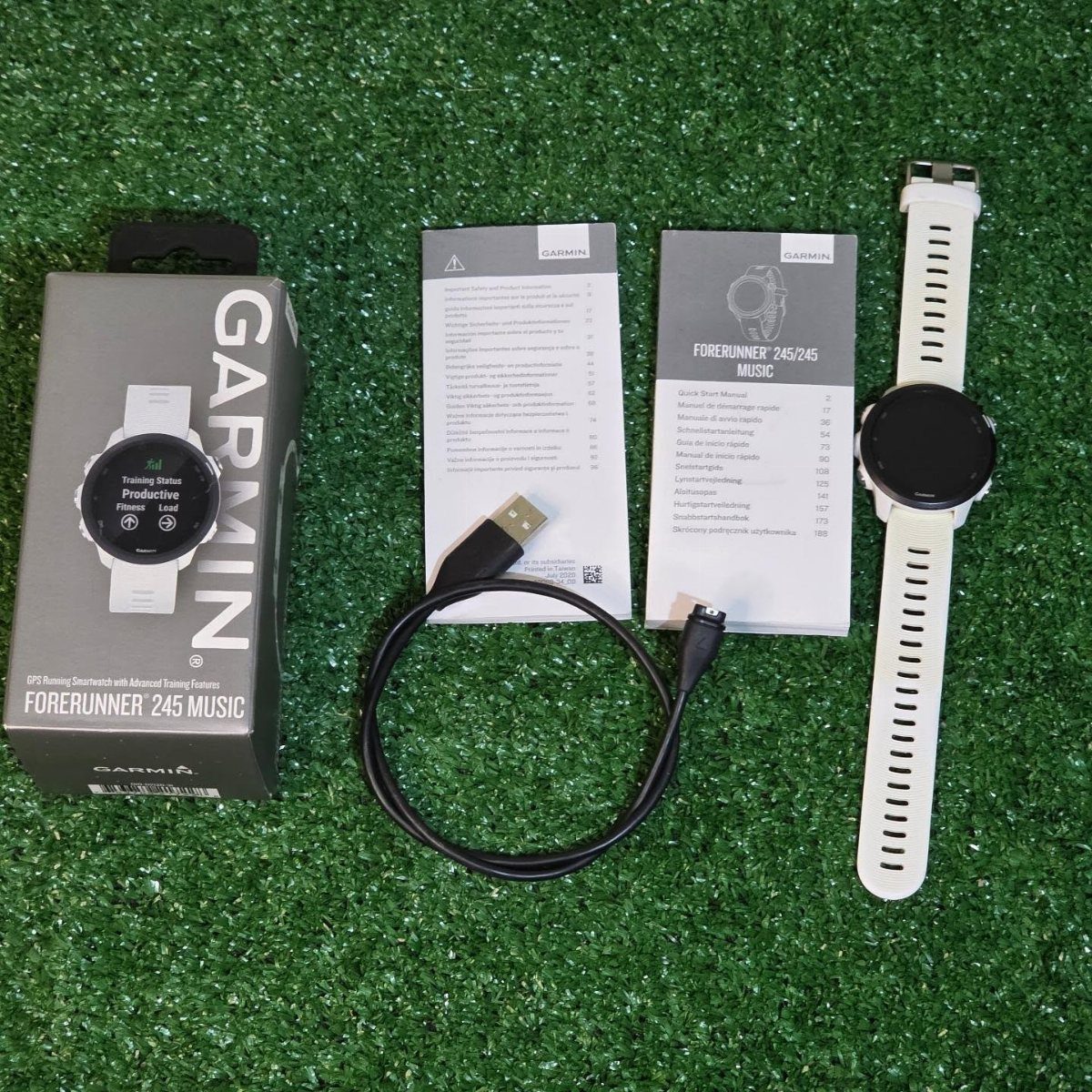 White Garmin Forerunner 245 Music watch with box and cable on green grass