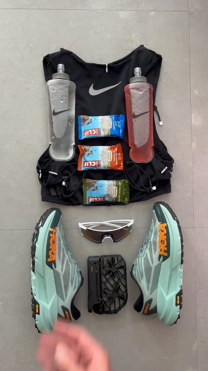Black Nike hydration vest with water bottles, Hoka shoes, and running sunglasses.
