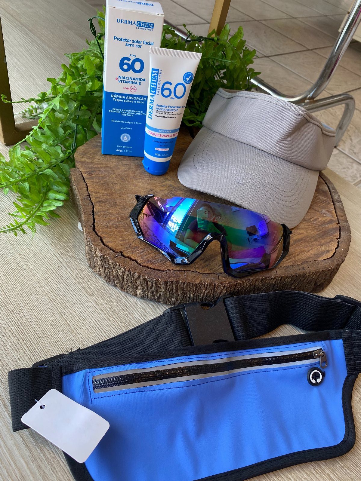 Sunscreen, iridescent sunglasses, a grey visor, and a blue running belt on wood.