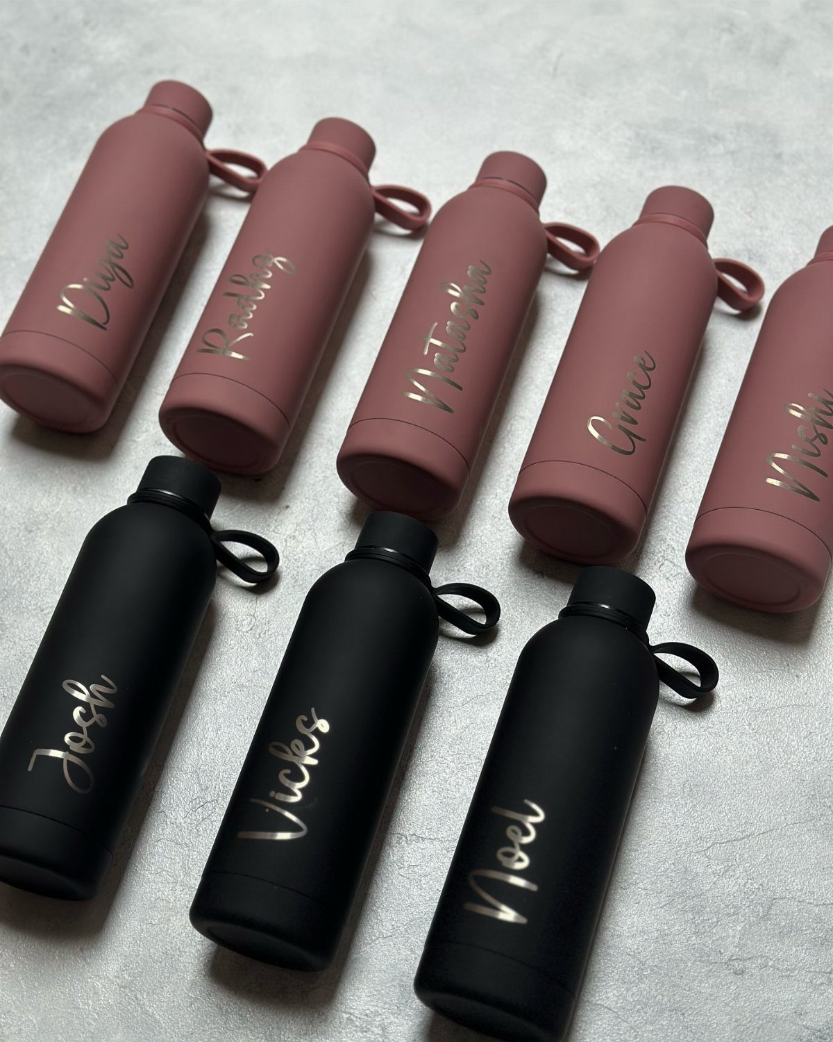 Personalized matte water bottles in dusty rose and black with gold cursive names.