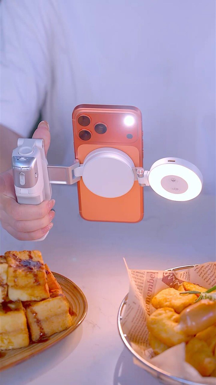 Orange smartphone with a white ring light attachment held over plates of food