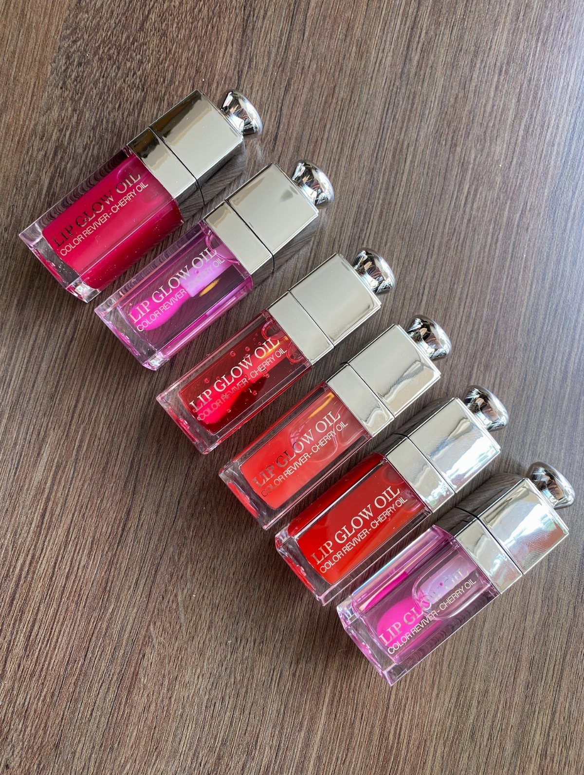 Six Dior Lip Glow Oil tubes in pink and red shades on wood.