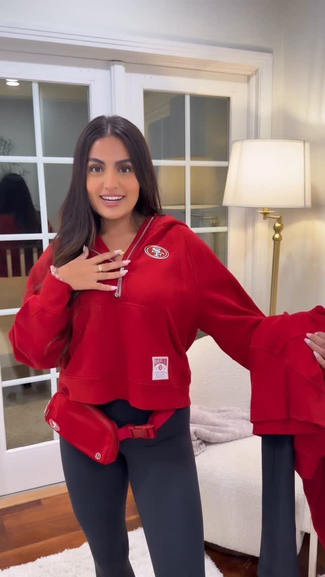 Woman wearing a red oversized half-zip hoodie and red waist bag indoors.