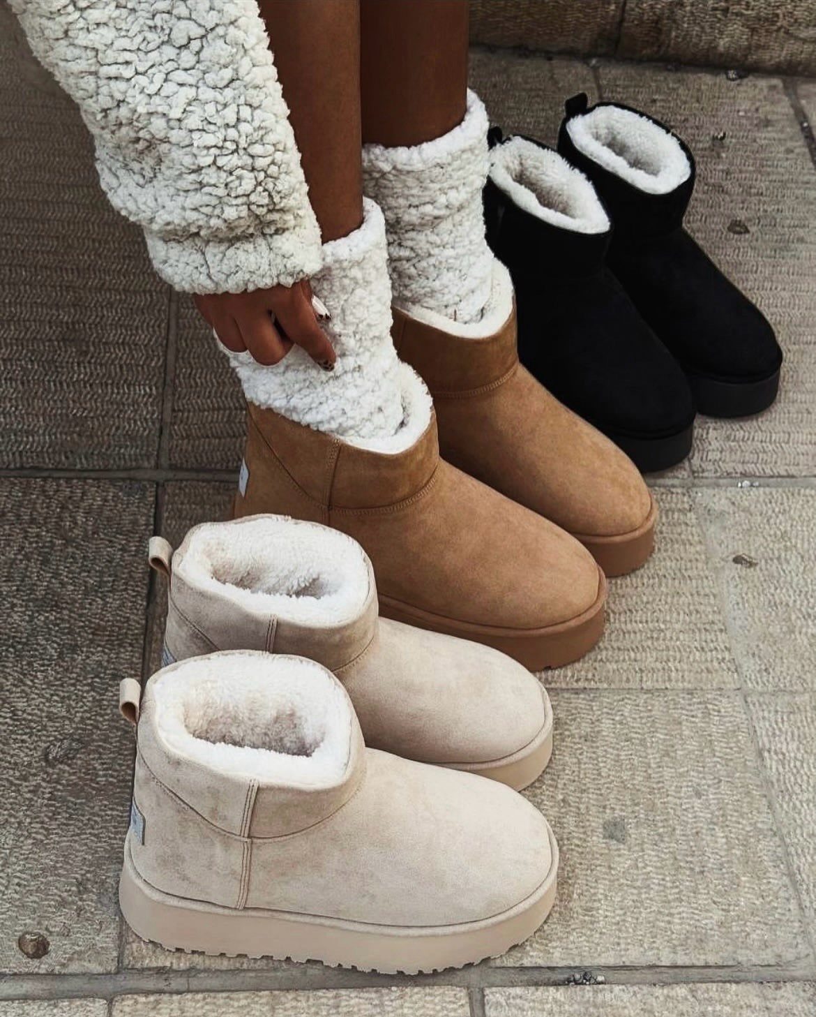 Sheepskin boots in tan, black, and cream colors on a stone pavement.