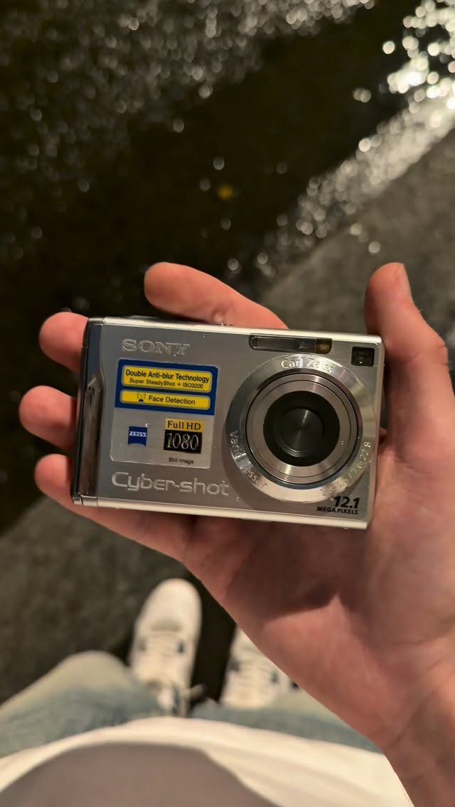 Silver Sony Cyber-shot digital camera held in a hand over shimmering dark water
