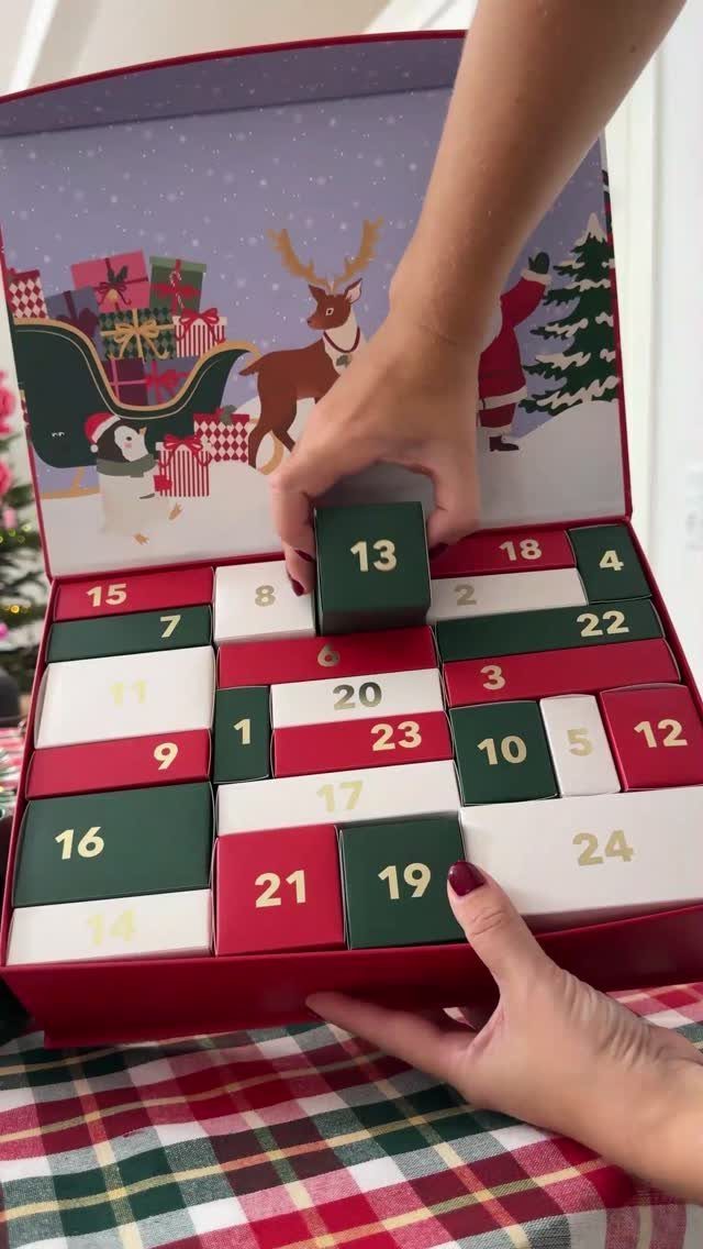 Hands opening a red advent calendar box with numbered colorful drawers and festive illustrations.