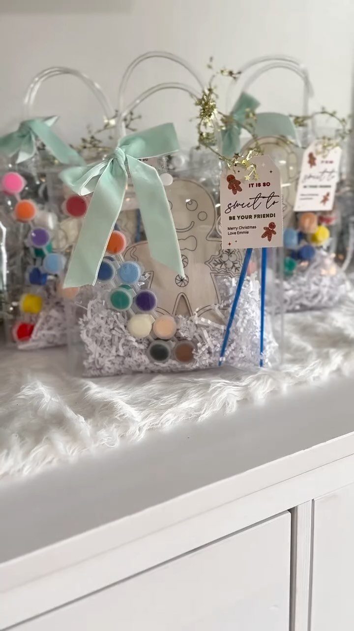 Clear gift bags containing colorful paint pots, brushes, and a gingerbread cutout.