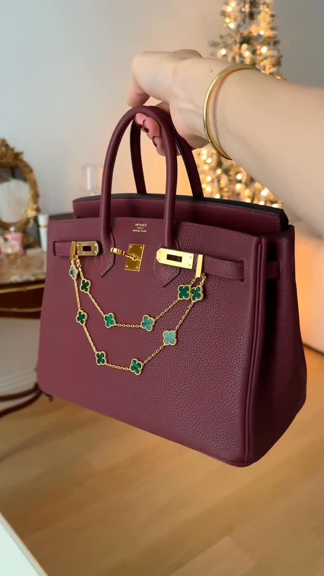 Burgundy leather handbag with gold clover chain held before a lit Christmas tree