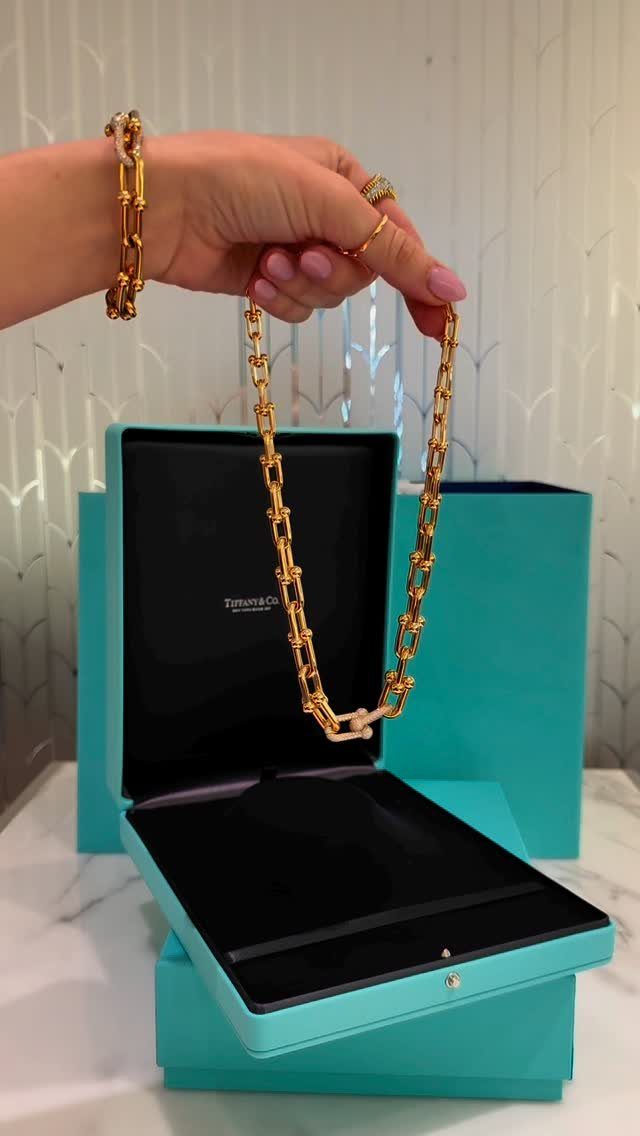 Gold chain necklace held over an open turquoise jewelry box by a hand.