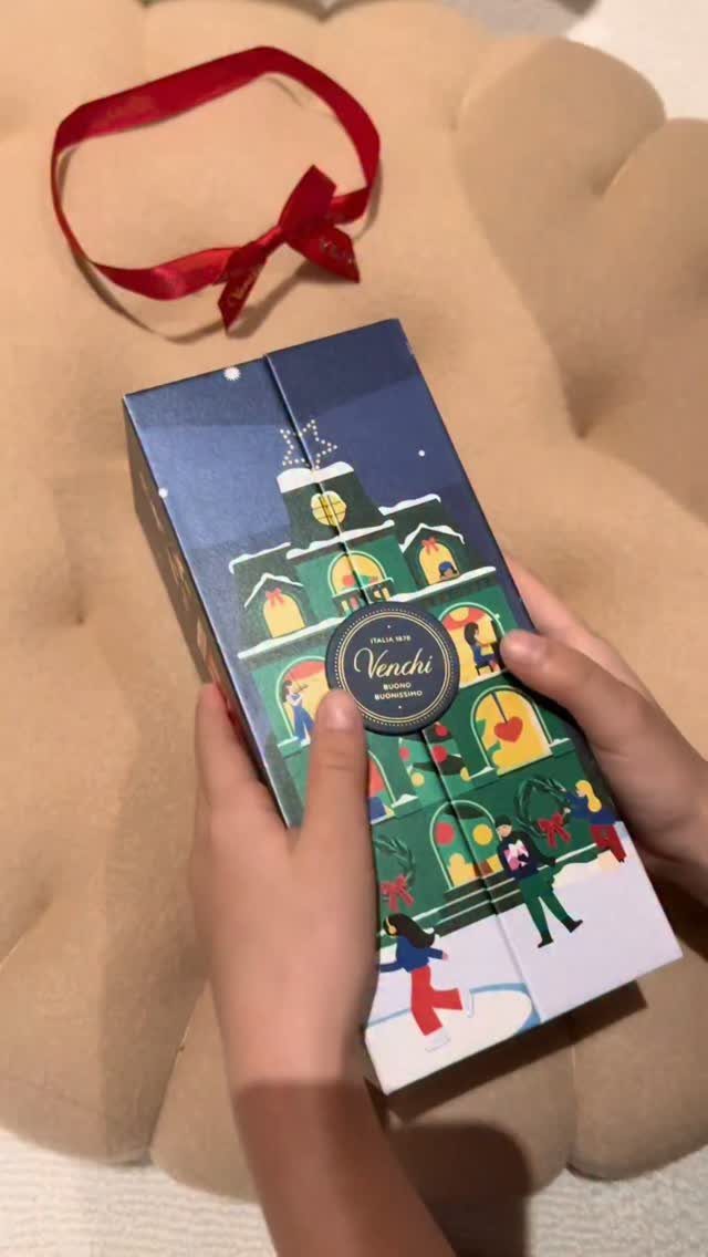 Hands holding a Venchi chocolate gift box with a winter village illustration.