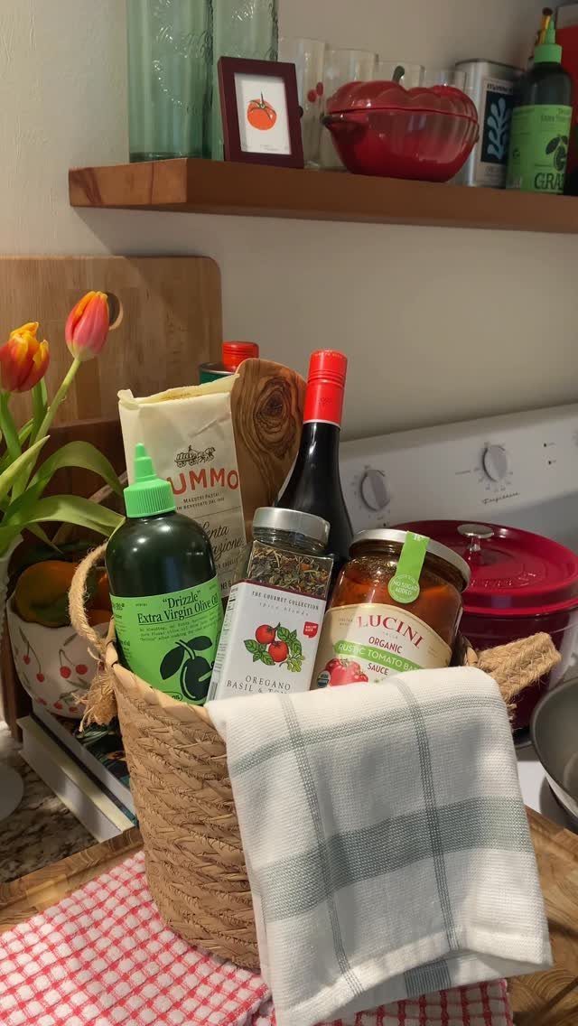 Woven gift basket containing olive oil, pasta sauce, and spices in a kitchen.