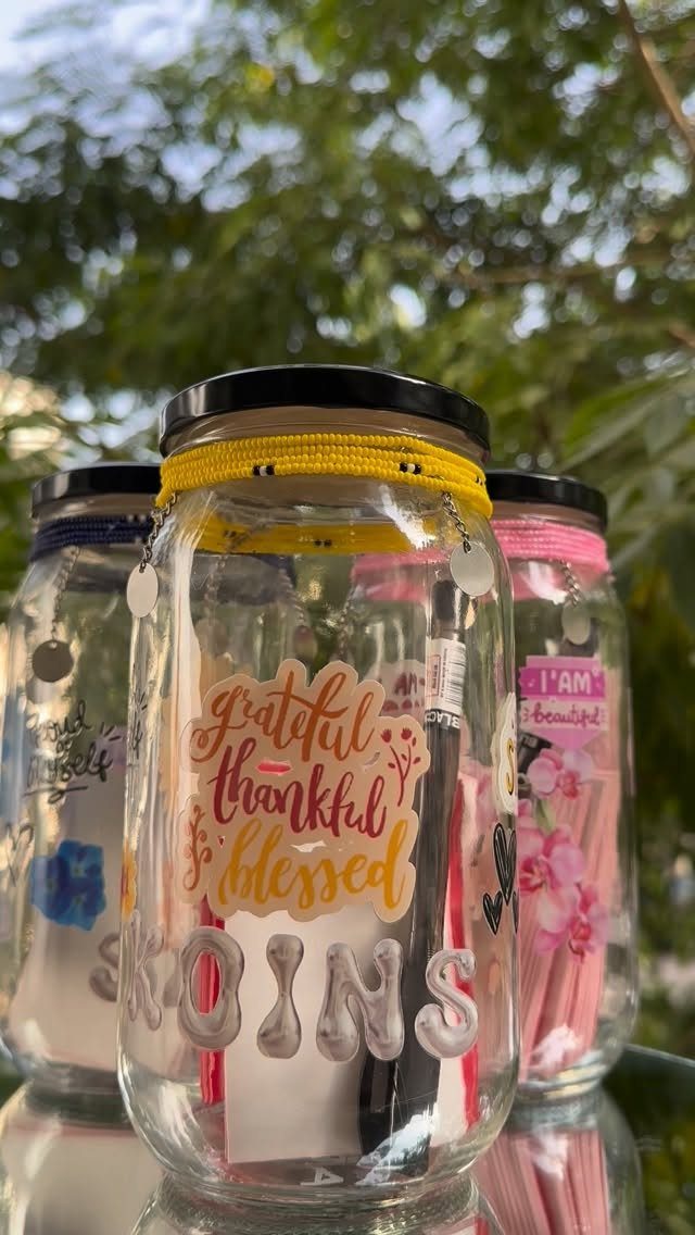 Glass gratitude jars with colorful decorations and notes, set against a blurred green background.