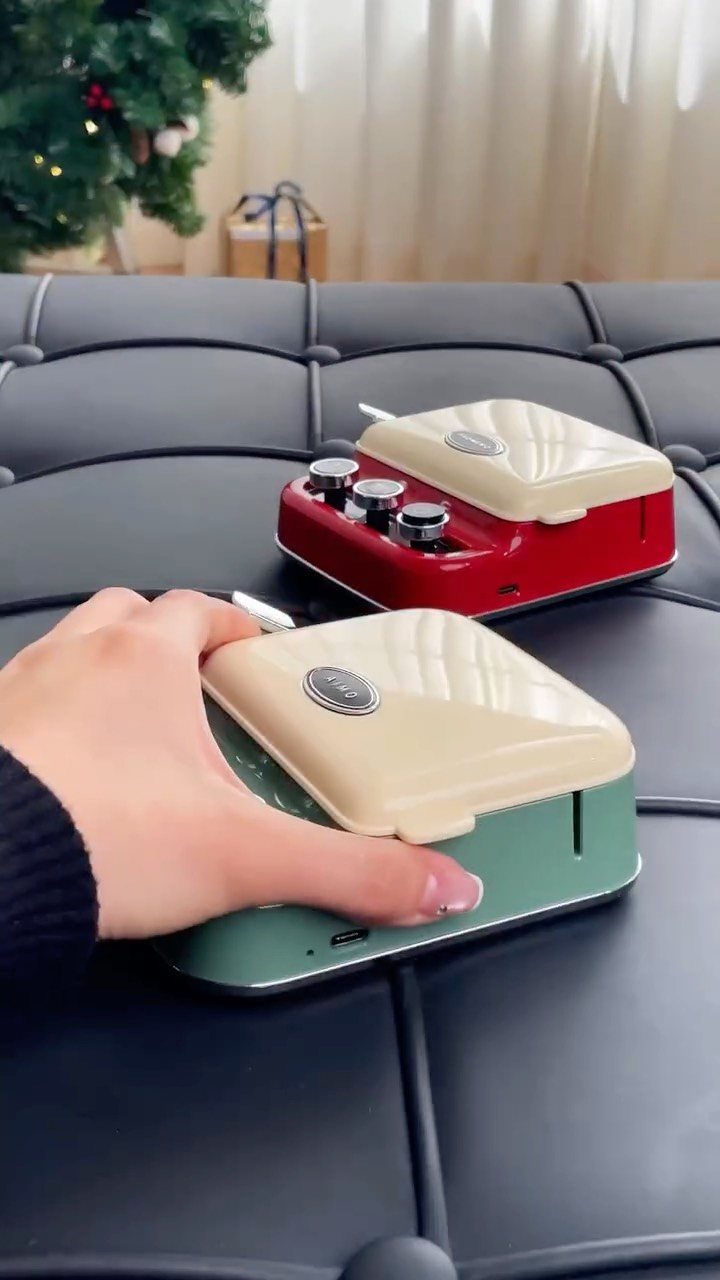 Mini waffle makers in mint green and red on a black leather surface.