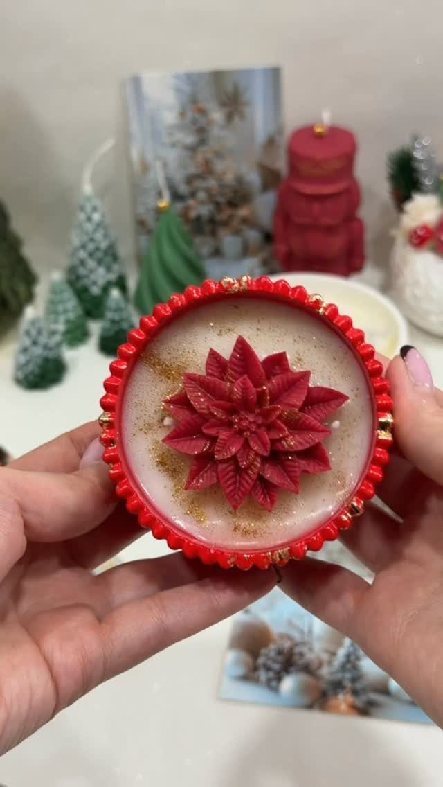 Red-rimmed candle with a red poinsettia flower held by two hands.