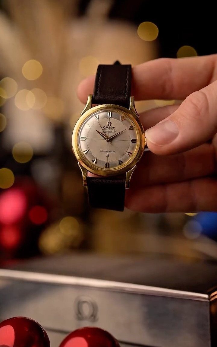 Gold Omega wristwatch with brown leather strap held against blurred Christmas lights