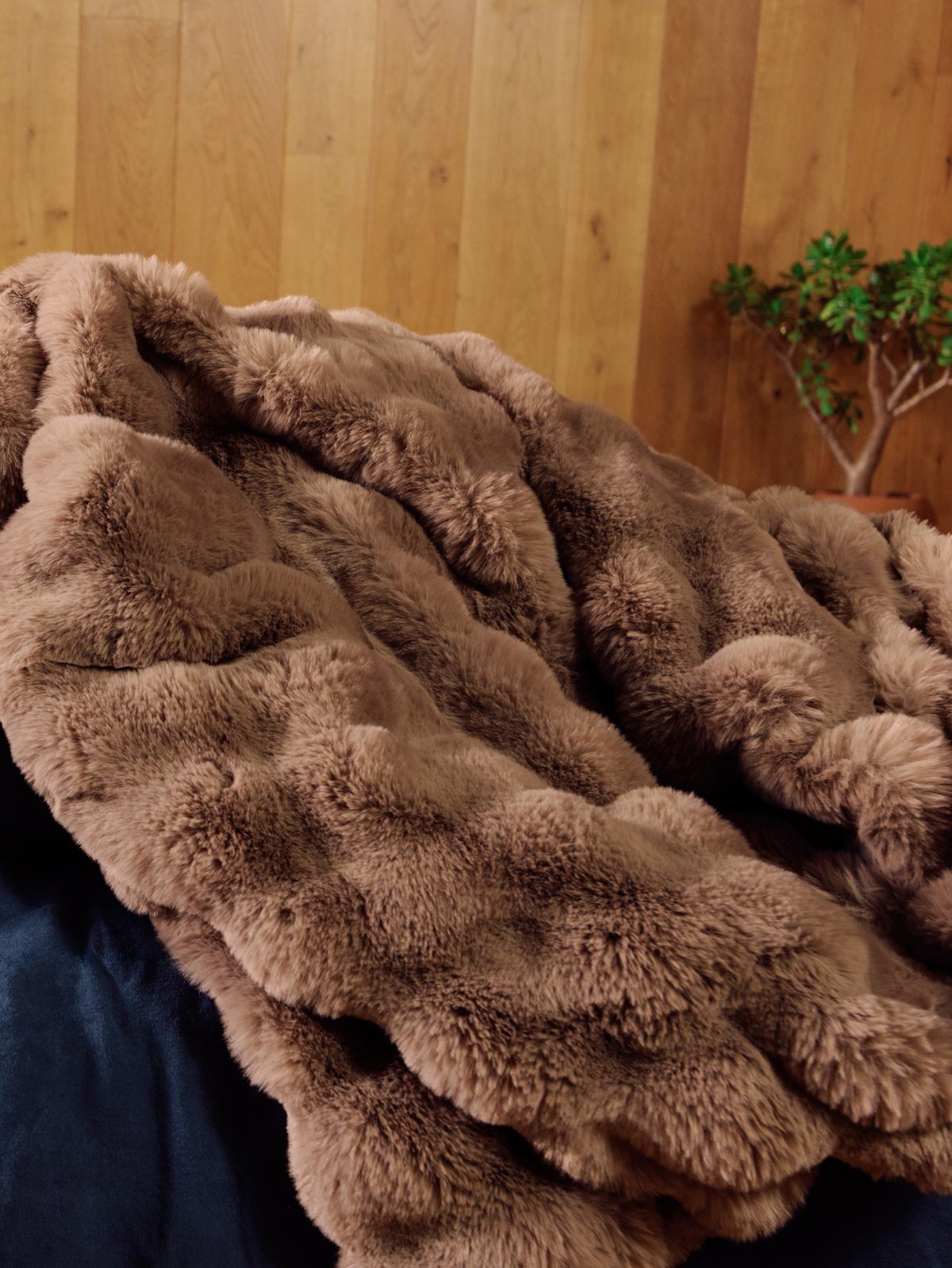 Brown fluffy faux-fur blanket draped over a dark blue surface against wooden walls.