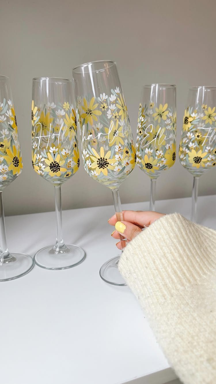 Champagne flutes with yellow floral designs and white script held by a person.