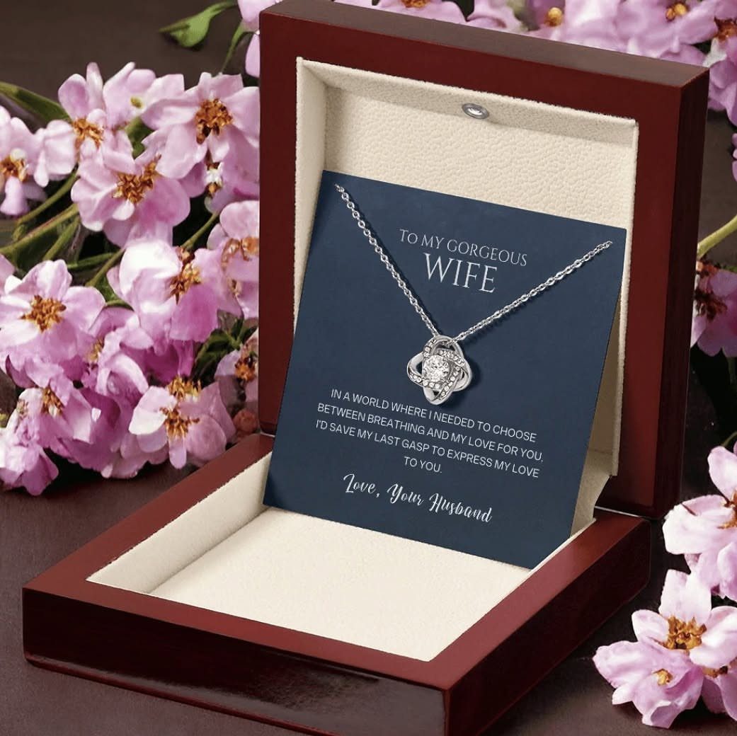 Silver love knot necklace in a red box surrounded by pink cherry blossoms