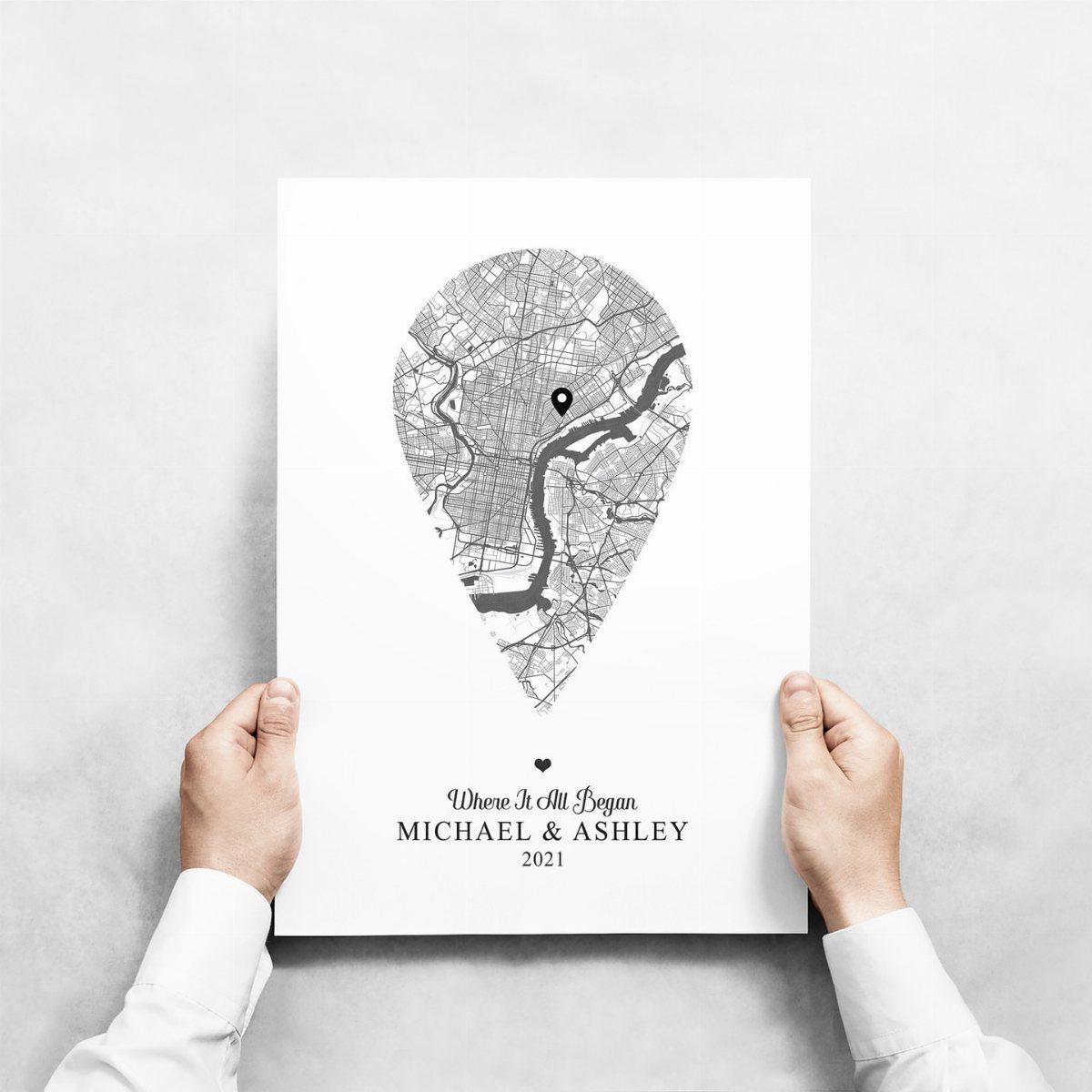Personalized city map poster shaped like a location pin held by two hands.
