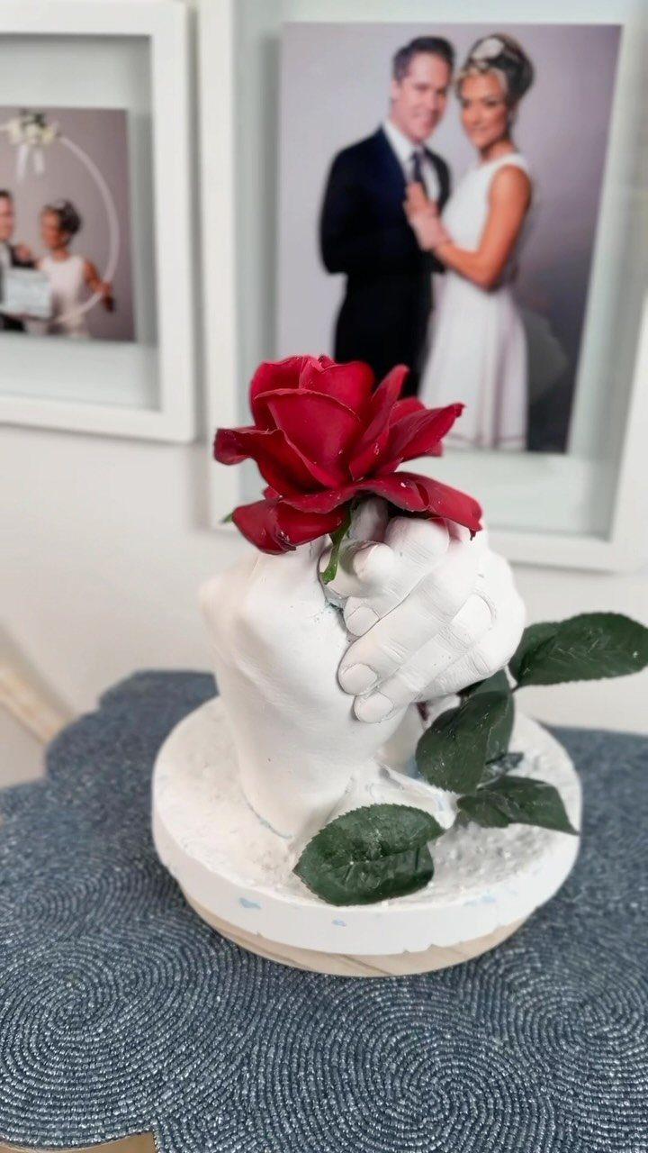 White plaster cast of holding hands with a red rose on top.