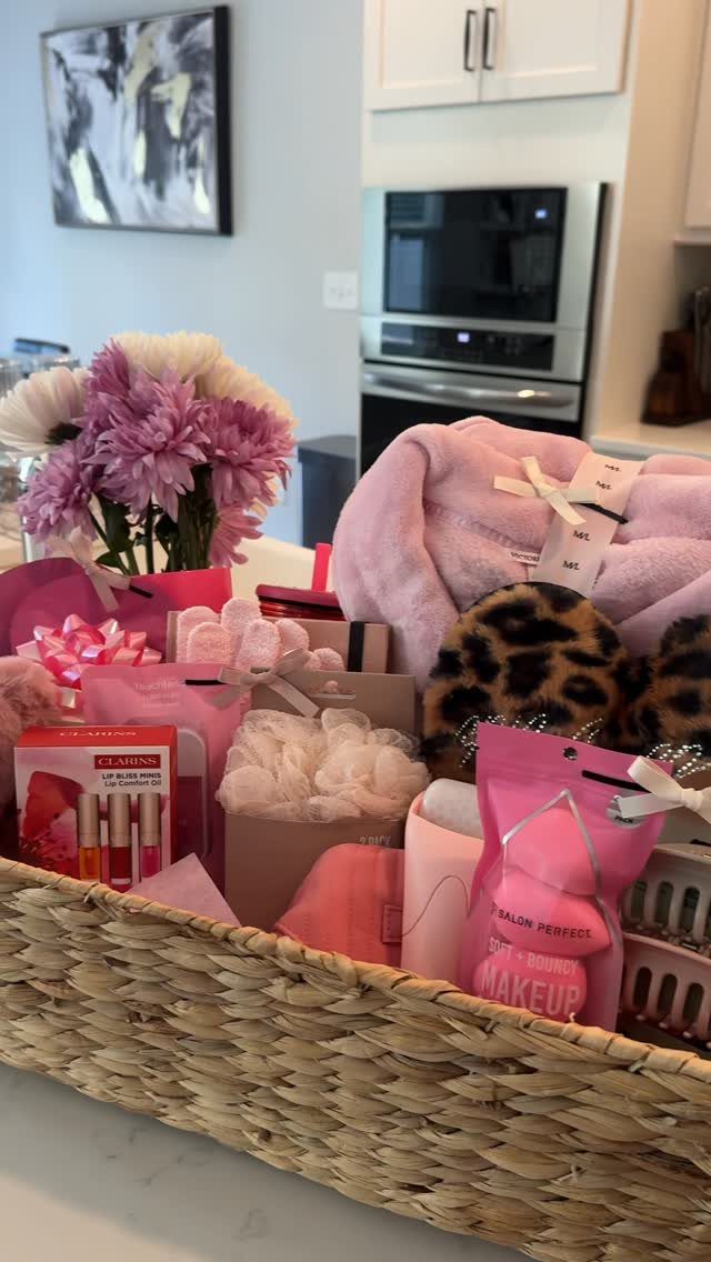 Woven basket filled with pink robe, leopard slippers, beauty products, and purple flowers.