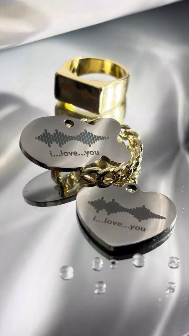 Silver heart and fish pendants with engraved soundwaves and love text beside gold jewelry.