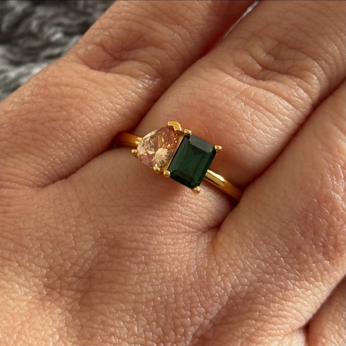 Gold ring with peach and green gemstones worn on a person's finger