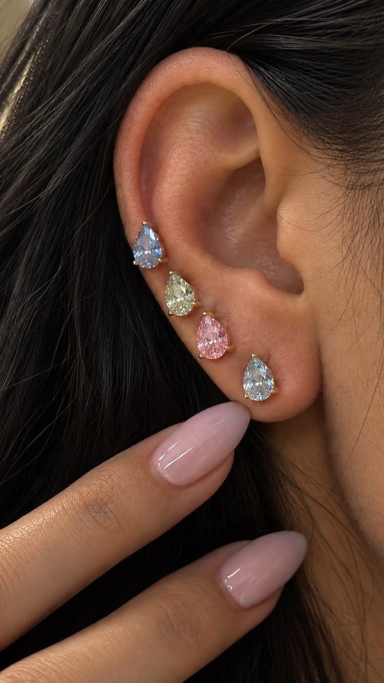 Ear with four colorful pear-shaped gemstone earrings and light pink manicured nails.