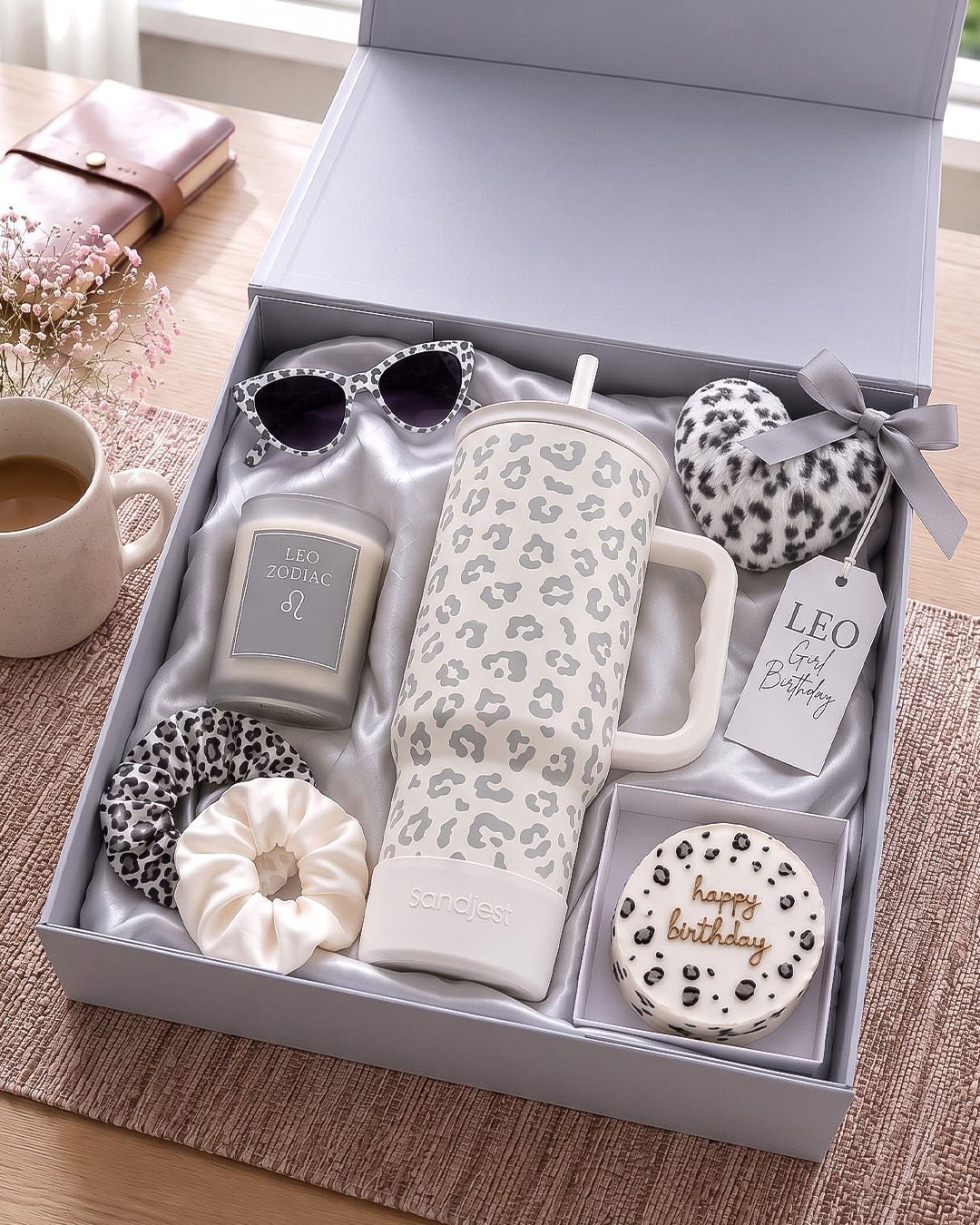 Gift box with leopard print tumbler, candle, sunglasses, and birthday treats on table